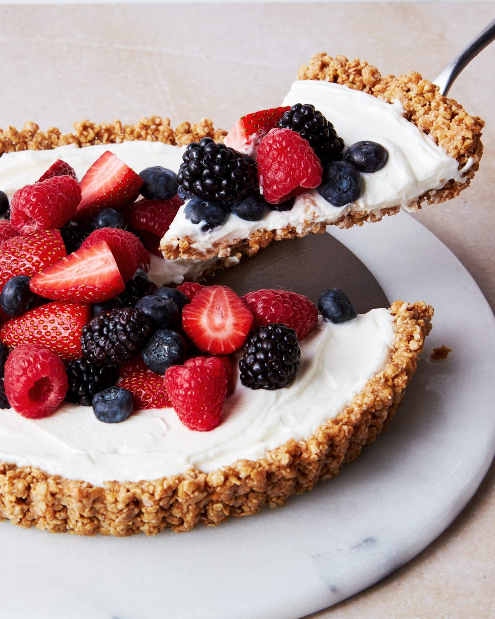 a slice of no bake fruit and granola breakfast tart topped with strawberries, blueberries, blackberries, and raspberries, coming out of the larger tart