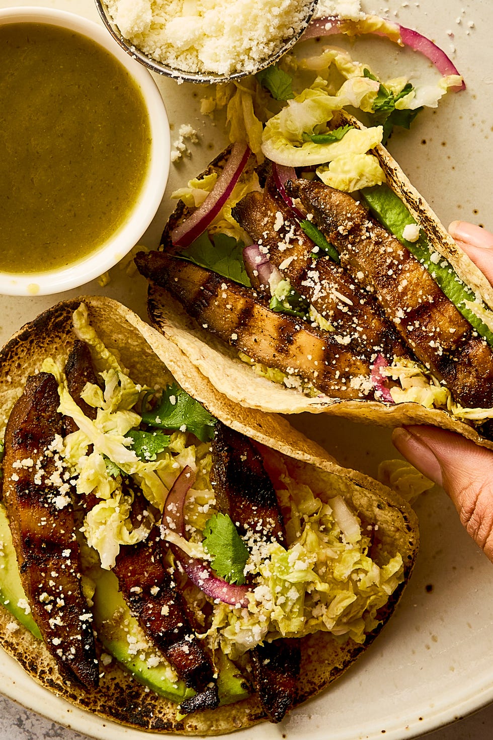 grilled portobello tacos topped with cabbage slaw, avocado, and queso fresco beside a bowl of salsa verde