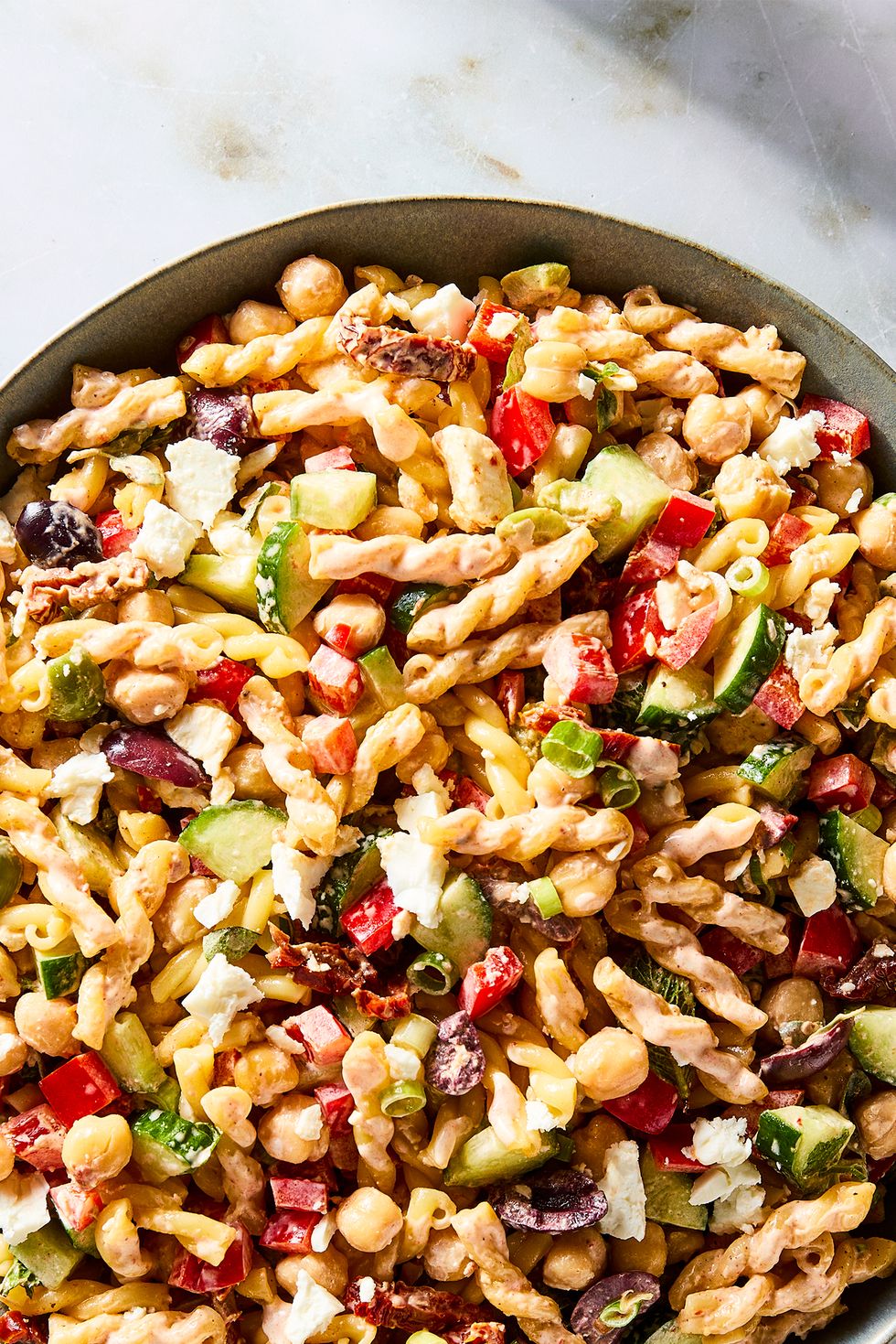 gemelli pasta tossed with chickpeas, bell pepper, cucumber, scallions, feta, olives, herbs, and tomatoes, then tossed in harissa mayo