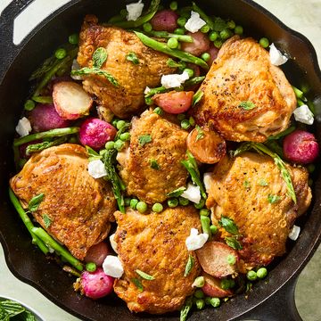 crispy chicken thighs in a cast iron skillet with radishes, asparagus, and peas