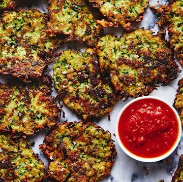 a tray of fried zucchini fritters with a bowl of marinara sauce