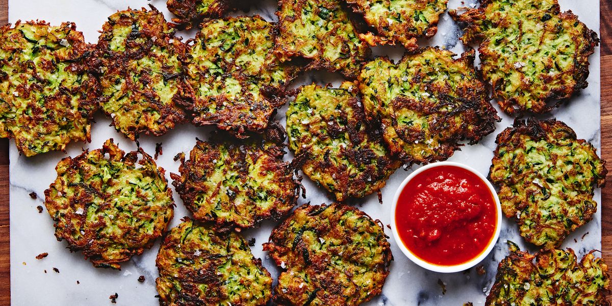 a tray of fried zucchini fritters with a bowl of marinara sauce