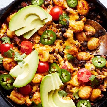 a pan with gnocchi covered in enchilada sauce, cheese, avocado, cilantro, and cherry tomatoes
