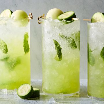 a glass filled with ice, rum, mint leaves, midori liqueur, and lime juice garnished with a cucumber slice and honeydew melon ball