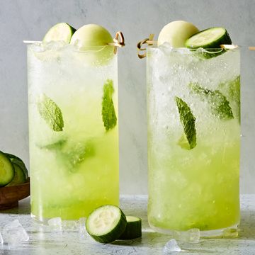 a glass filled with ice, rum, mint leaves, midori liqueur, and lime juice garnished with a cucumber slice and honeydew melon ball