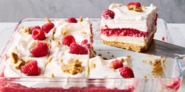 a slice of no bake raspberry cheesecake lasagna lifting out of the larger cheesecake lasagna in a glass pan