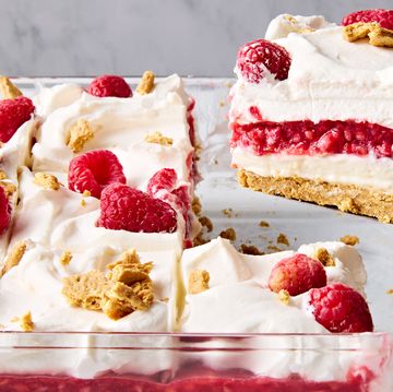 a slice of no bake raspberry cheesecake lasagna lifting out of the larger cheesecake lasagna in a glass pan
