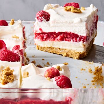 a slice of no bake raspberry cheesecake lasagna lifting out of the larger cheesecake lasagna in a glass pan