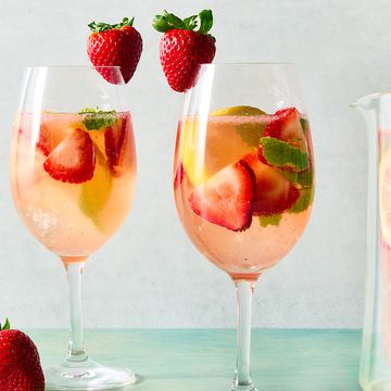 a pitcher and glasses of sangria made with white wine and strawberry syrup with ice, pieces of mint, sliced strawberry, and sliced lemons