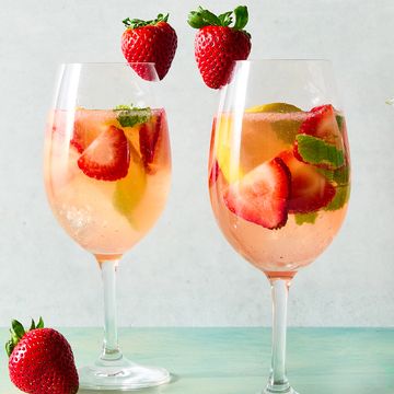 a pitcher and glasses of sangria made with white wine and strawberry syrup with ice, pieces of mint, sliced strawberry, and sliced lemons
