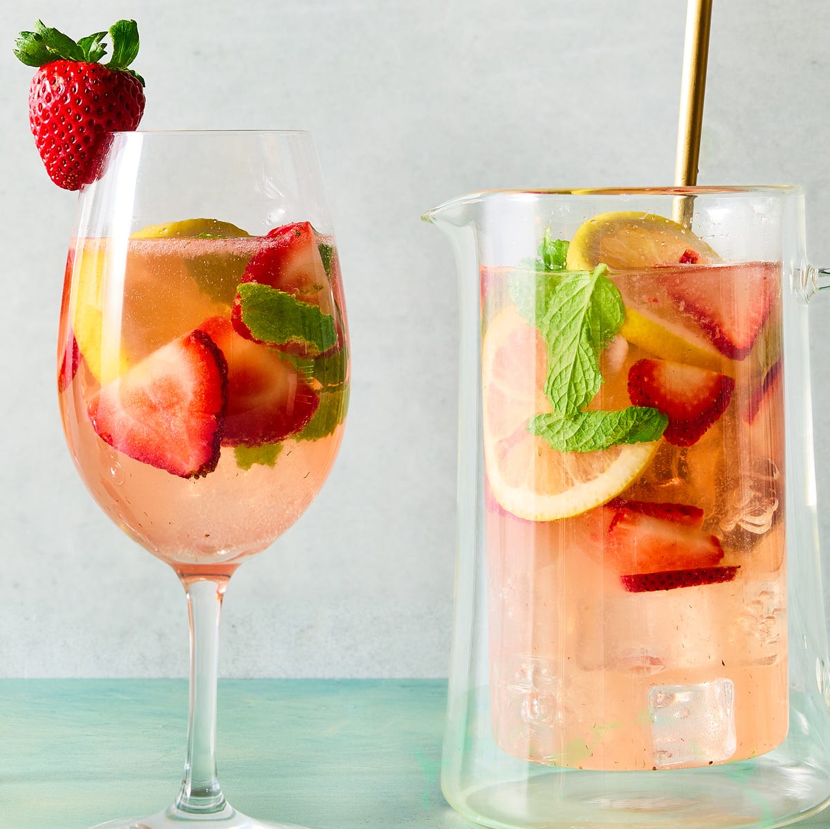 Strawberry Mint Sangria a pitcher and glasses of sangria made with white wine and strawberry syrup with ice, pieces of mint, sliced strawberry, and sliced lemons