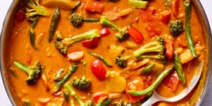 a pot of thai style curry in a coconut milk broth with broccoli, potatoes, carrots, and peppers