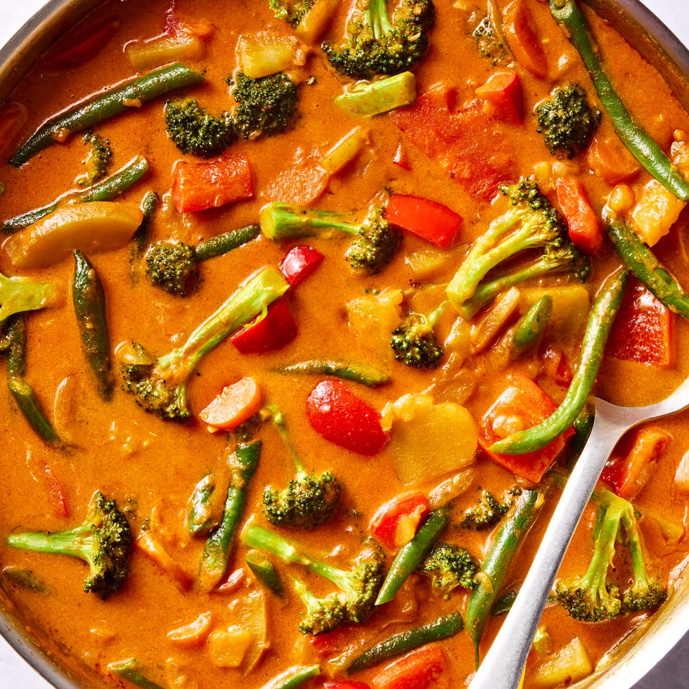 a pot of thai style curry in a coconut milk broth with broccoli, potatoes, carrots, and peppers