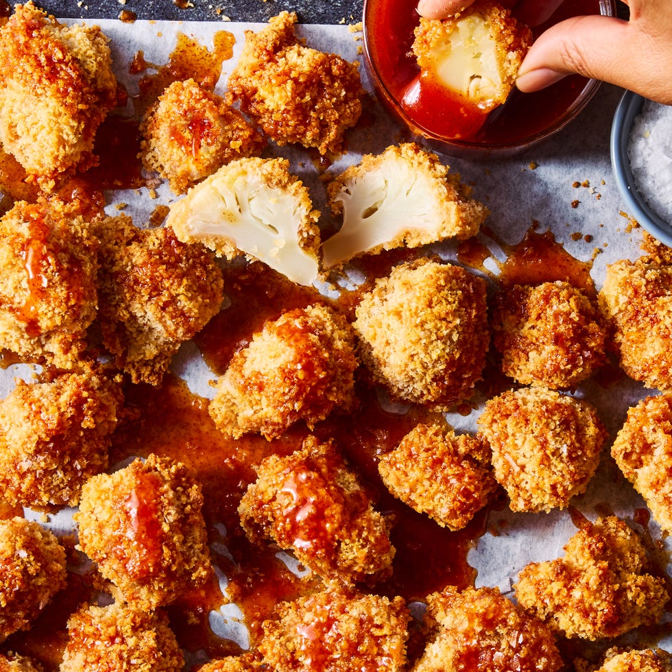 crispy hot honey cauliflower nuggets on white parchment paper with one being dipped into sauce