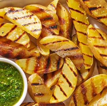 grilled potatoes on a white platter with a bowl of green herb sauce