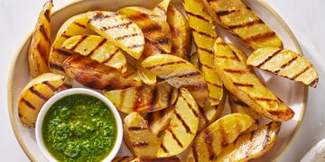 grilled potatoes on a white platter with a bowl of green herb sauce