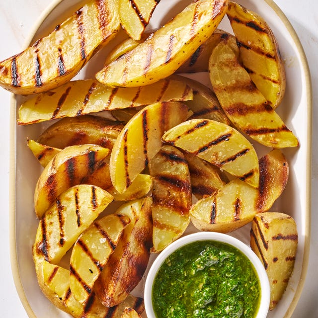 grilled potatoes on a platter with a ramekin of herby green sauce