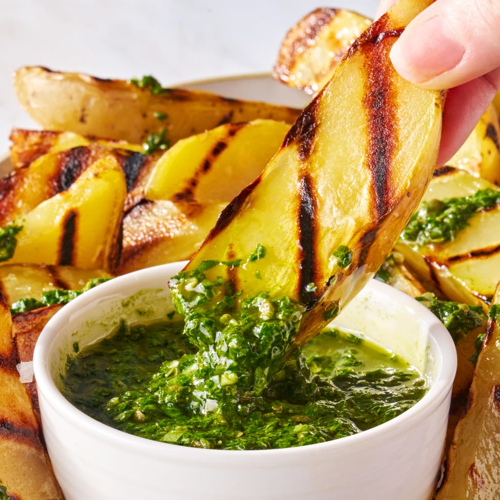 a grilled potato being dunked into a bowl of herby green sauce