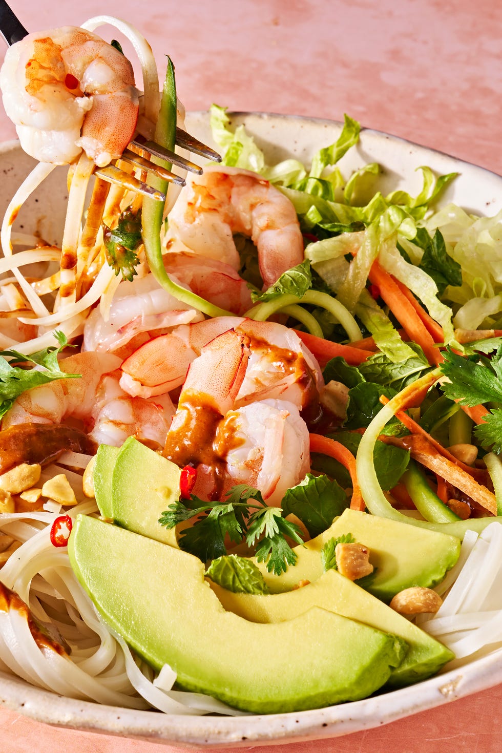 Summer roll bowl fork lifting a bite of summer roll bowl with rice noodles, shrimp, avocado, and peanuts