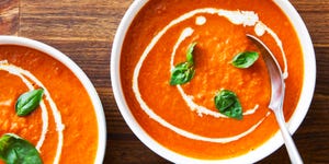 two bowls of tomato soup topped with basil and swirls of cream
