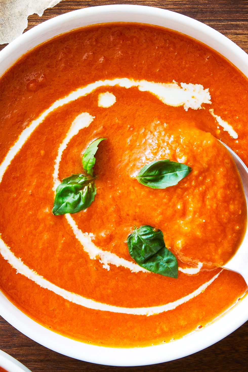 bowl of tomato soup topped with basil and swirls of heavy cream beside grilled cheese