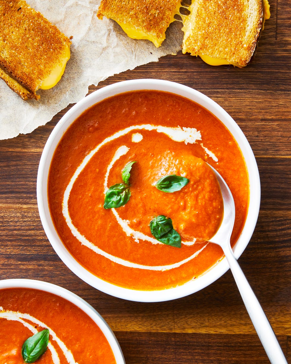 bowl of tomato soup topped with basil and swirls of heavy cream beside grilled cheese