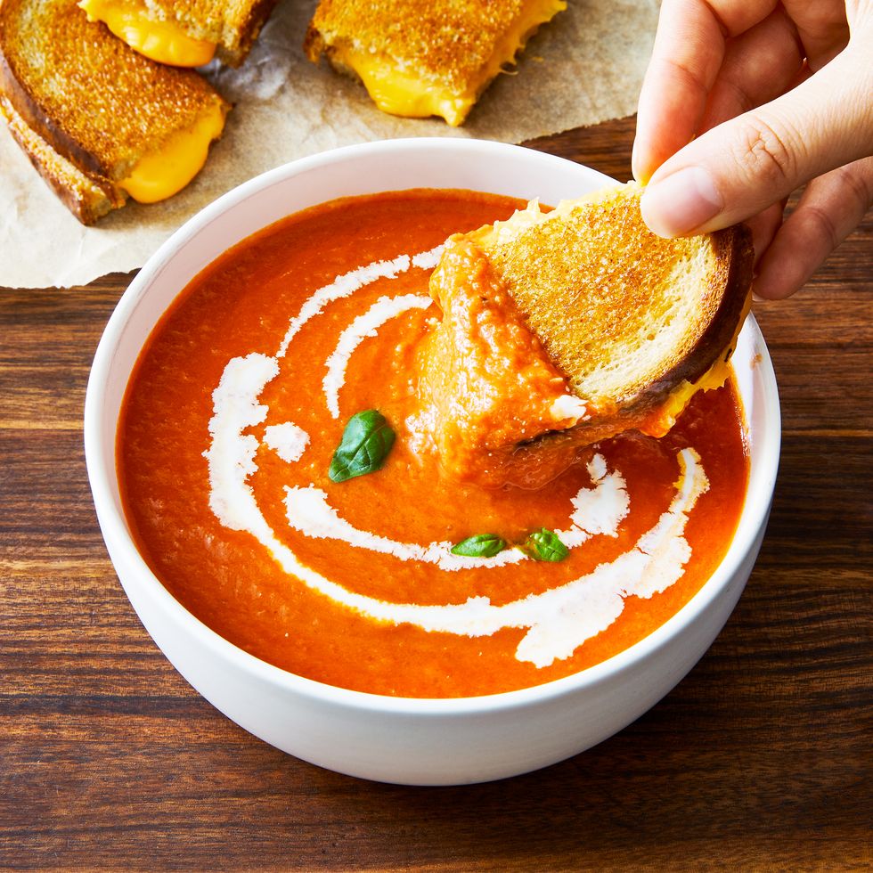 bowl of tomato soup with a piece of grilled cheese sandwich being dunked into it