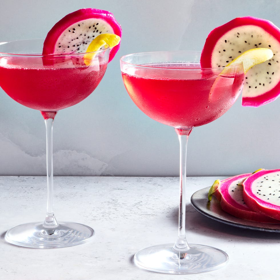 two coupe glasses filled with a bright pink vodka based cocktail and garnished with a slice of dragon fruit and a lemon twist