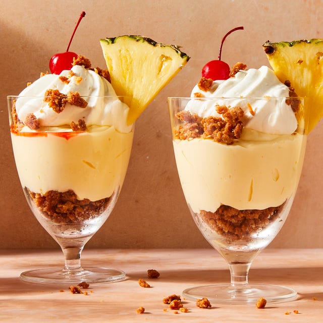 pina colada mousse layered with coconut oat crunch in glass parfait cups topped with whipped cream and a cherry