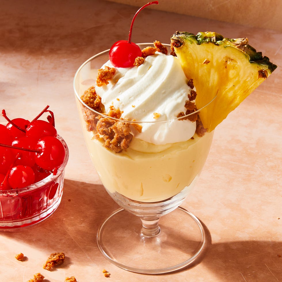 pina colada mousse layered with coconut oat crunch in glass parfait cups topped with whipped cream and a cherry