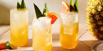 glasses filled with grapefruit juice, pineapple juice, tequila, and soda water garnished with a grapefruit wedge, pineapple leaves, and a salted rim
