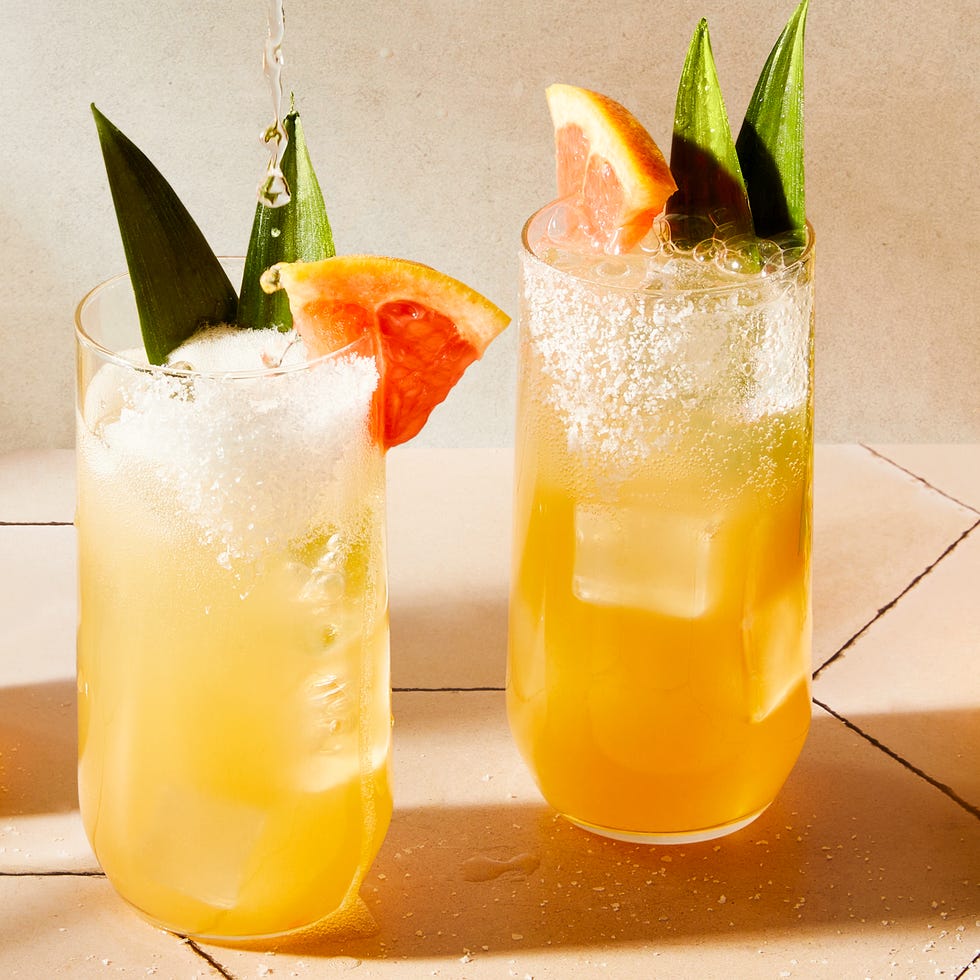 glasses filled with grapefruit juice, pineapple juice, tequila, and soda water garnished with a grapefruit wedge, pineapple leaves, and a salted rim