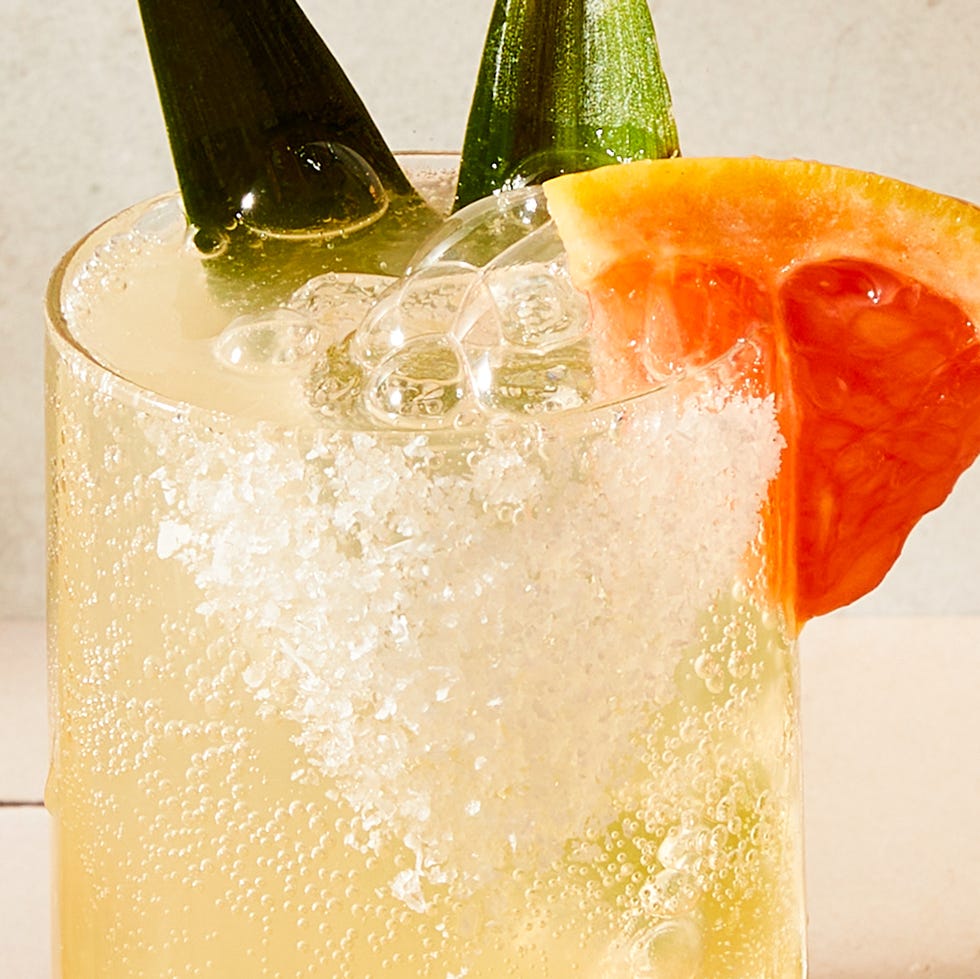 glasses filled with grapefruit juice, pineapple juice, tequila, and soda water garnished with a grapefruit wedge, pineapple leaves, and a salted rim
