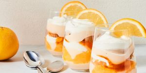 a stemless wine glass filled with vanilla cake, whipped cream, aperol spiked jam, and pudding with an orange slice on the rim