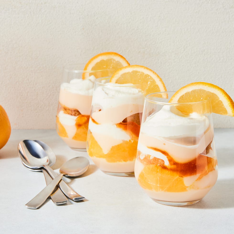 a stemless wine glass filled with vanilla cake, whipped cream, aperol spiked jam, and pudding with an orange slice on the rim