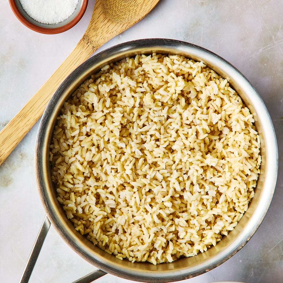 a pot of brown rice beside a wooden spoon and a pinch bowl of salt