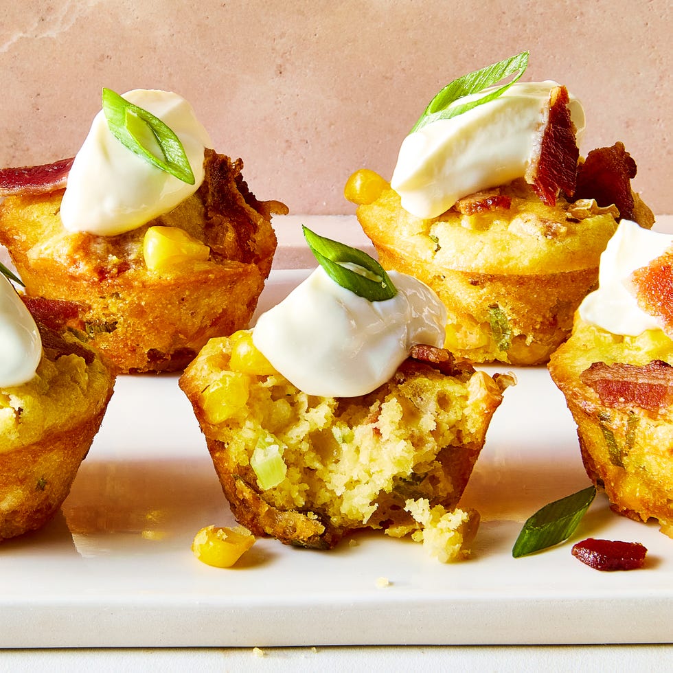 loaded cheesy corn bites on a white plate topped with sour cream, sliced scalllion, and bacon