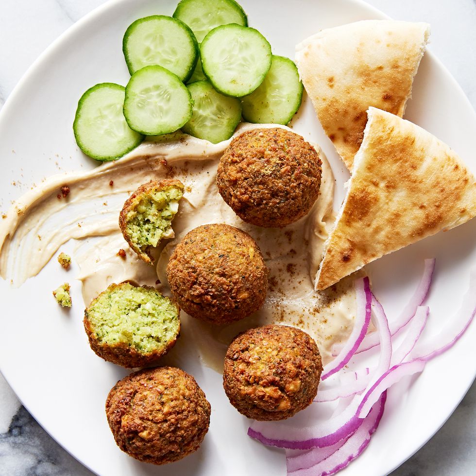 falafel on a plate with pita, red onion, cucumber, and tahini sauce