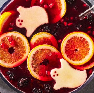 a bowl of red wine based punch with ice cubes, blackberries, pomegranate seeds, and green apple slices cut to resemble ghosts