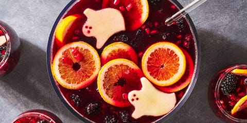 a bowl of red wine based punch with ice cubes, blackberries, pomegranate seeds, and green apple slices cut to resemble ghosts