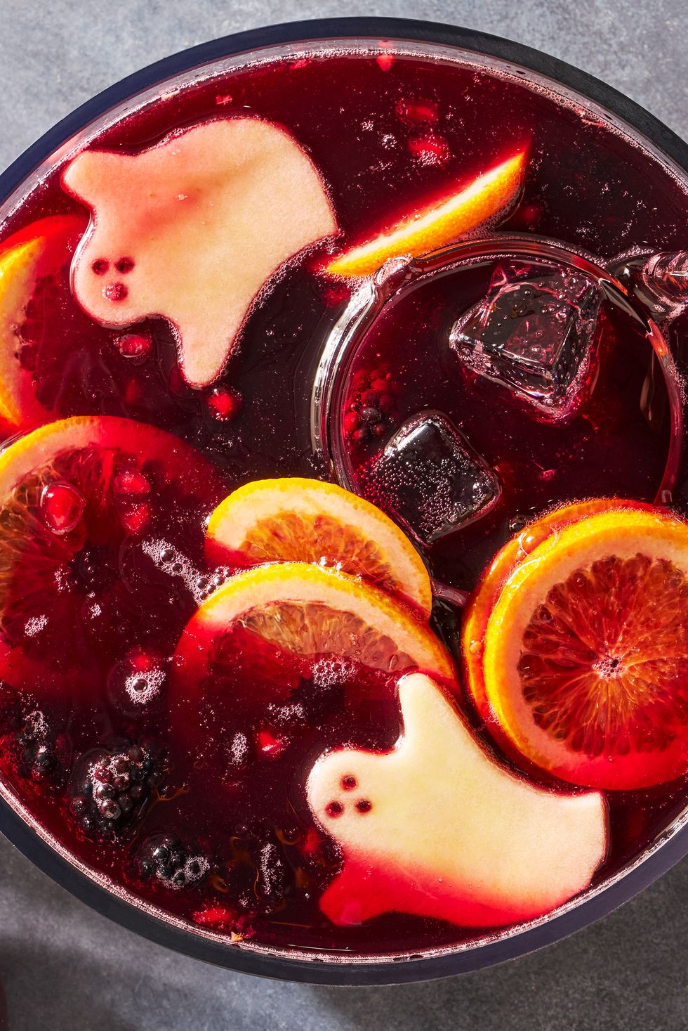 a bowl of red wine based punch with ice cubes, blackberries, pomegranate seeds, and green apple slices cut to resemble ghosts