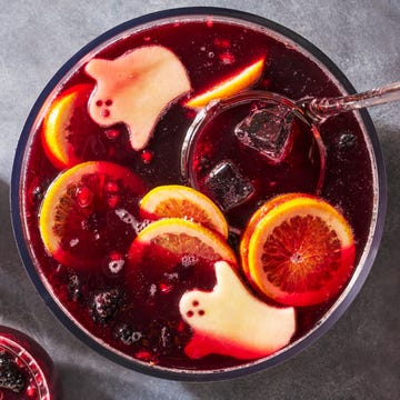 a bowl of red wine based punch with ice cubes, blackberries, pomegranate seeds, and green apple slices cut to resemble ghosts