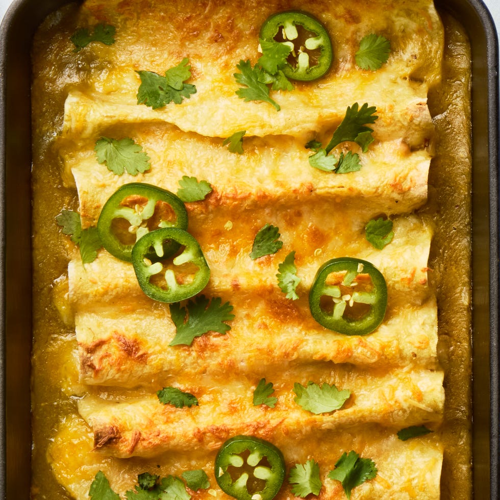 green chili white bean enchiladas topped with cheese, cilantro, and jalapenos in a black casserole pan