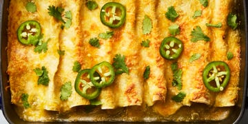 green chili whtie bean enchiladas topped with cheese, cilantro, and jalapenos in a cast iron casserole dish