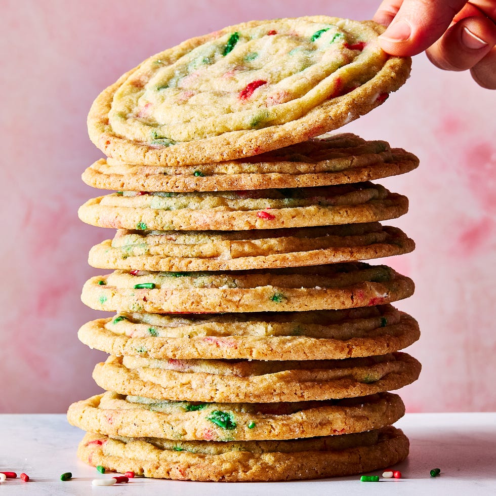 a stack of pan banging holiday confetti cookies with a hand lifting one off the top
