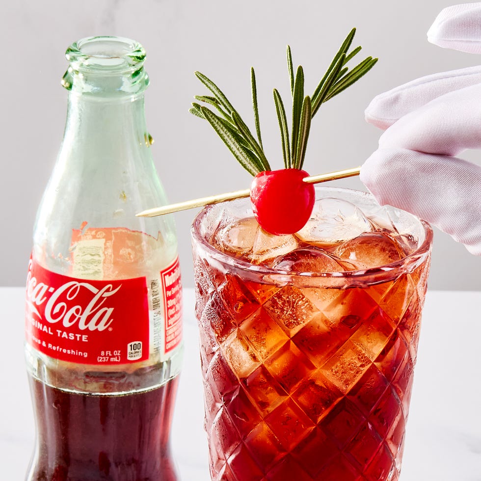 two glasses filled with ice, rum, cherry juice, and cola, garnished with a maraschino cherry decorated with two sprigs of rosemary