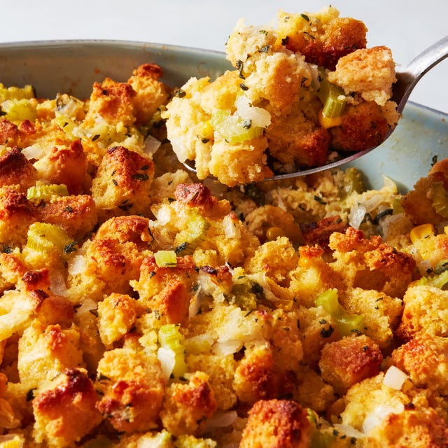 a spoon of cornbread stuffing lifted above an oval casserole dish