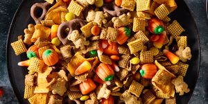 a bowl of halloween themed chex mix with chex cereal, chocolate pretzels, reese's pieces, candy corn, and sweet potato chips