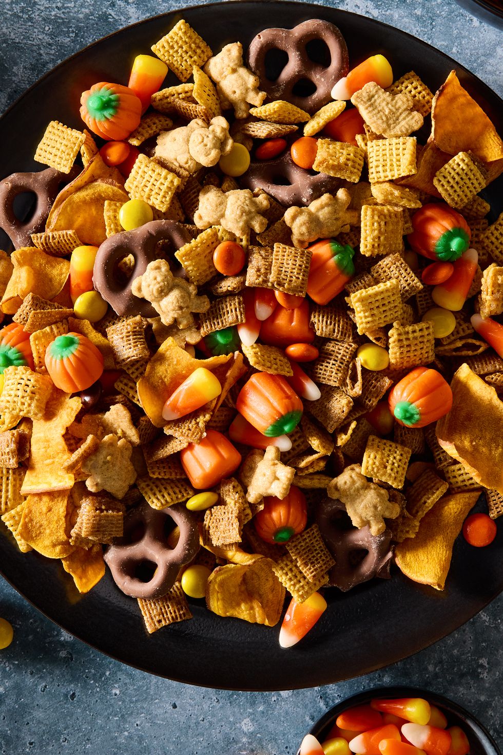 a bowl of halloween themed chex mix with chex cereal, chocolate pretzels, reese's pieces, candy corn, and sweet potato chips