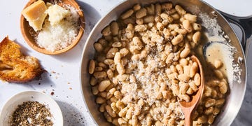 cacio e pepe white beans skillet with a wooden spoon beside a plate of cheese